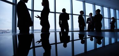 Group of colleagues standing against window in office and speaking